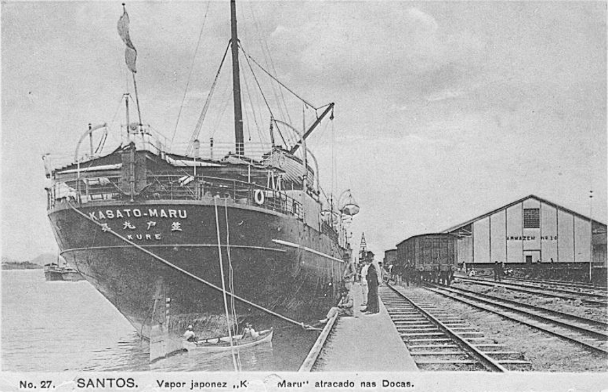 Cartão postal de época mostrando o navio Kasato Maru atracado no cais do porto de Santos, com pessoas na doca, 1908.
